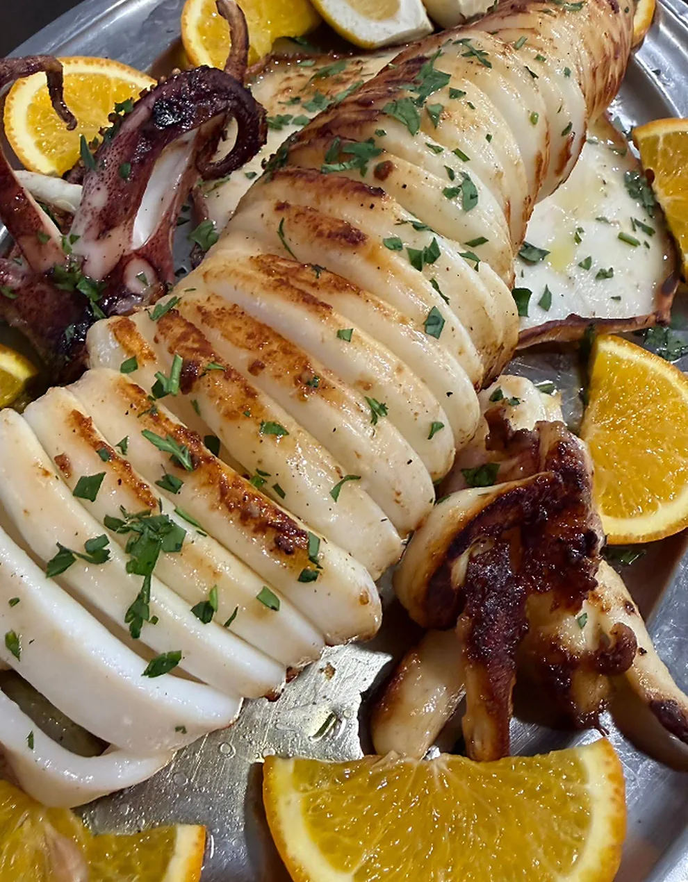Calamar entero a la plancha cortado en anillas, con perejil y rodajas de naranja