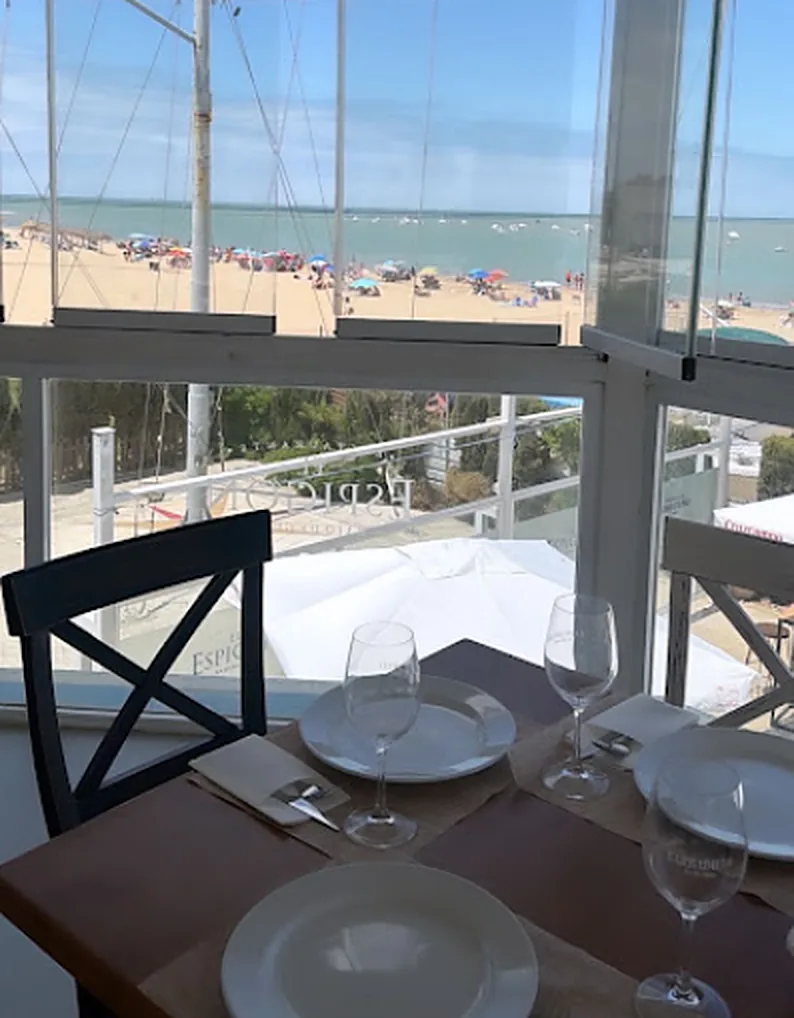 Mesa montada junto al cristal con la playa de Bajo de Guía llena de sombrillas al fondo